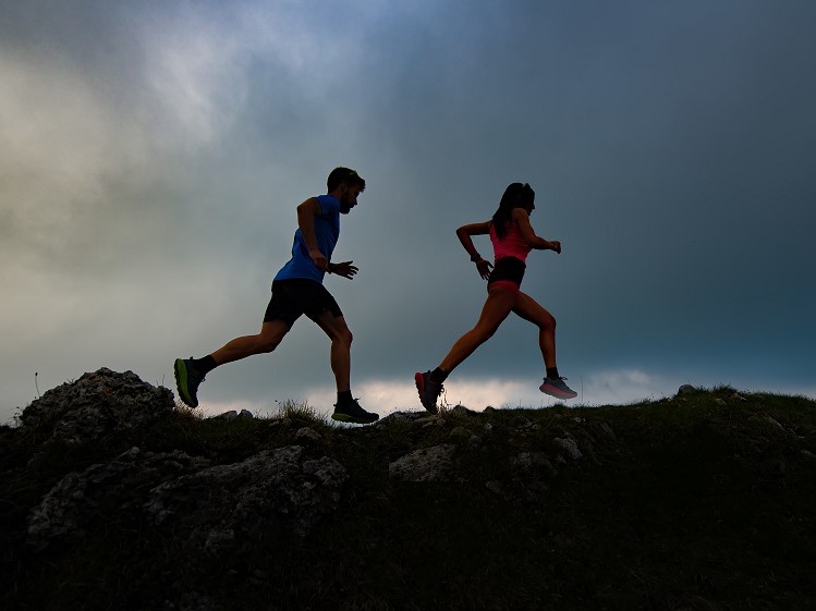 Couple of mountain runners man and woman train at sunset on a rocky ridge